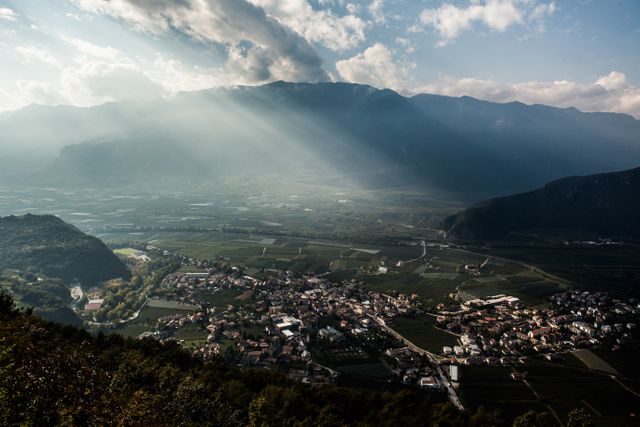 Sun rays piercing through clouds, illuminating a picturesque valley with a quaint village nestled below. Ideal for use in travel brochures, nature and landscape blogs, or relaxation and meditation content.