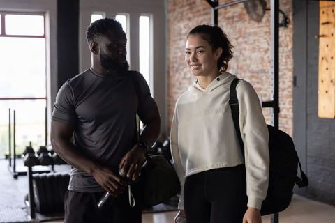 Diverse friends leaving gym carrying bags and water bottles after strength training