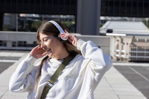 Young woman adjusting wireless headphones while enjoying sunny city rooftop plaza