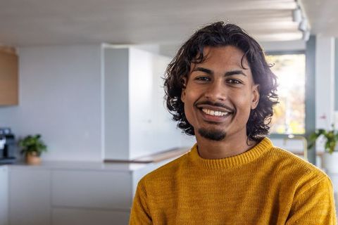 Smiling young asian man wearing mustard sweater in modern minimalist kitchen interior