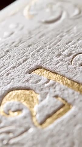 Vertical macro revealing embossed gold foil on textured cardstock with metallic ornament