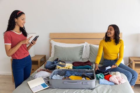 Mother and teen daughter packing luggage while checking smartphone in bright bedroom