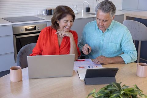 Senior couple reviewing finances planning retirement at home with laptop tablet and charts