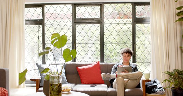 Young Man Relaxing on Sofa Using Tablet in Bright Living Room - Download Free Stock Images Pikwizard.com