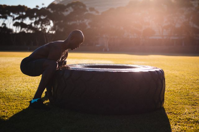 African American man lifting a large tire outdoors during sunset. Ideal for promoting fitness, strength training, and active lifestyle. Suitable for use in advertisements for gyms, fitness programs, and health-related content.