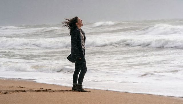 Windblown woman shouting at stormy ocean, standing on wet sand with crashing waves