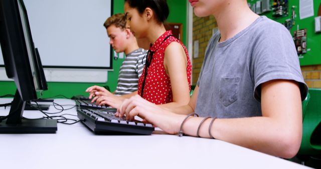 Three teenagers are sitting at desks, working on computers in a modern classroom. They appear focused on their tasks. This image can be used for educational content, technology in education, student learning environments, or articles on the importance of computer literacy among teenagers.