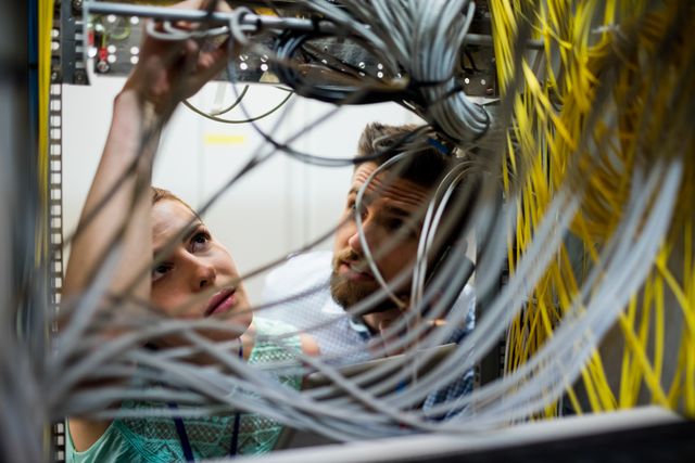 Technicians working on cables in a server room, ensuring proper network connectivity and maintenance. Ideal for use in articles about IT infrastructure, network maintenance, technical support, and data center operations.