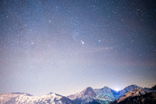 Wonderful depiction of a starry night sky over a snow-capped mountain range. Perfect for use in tourism advertisements, nature blogs, astronomy articles, wallpapers, and outdoor adventure promotions.