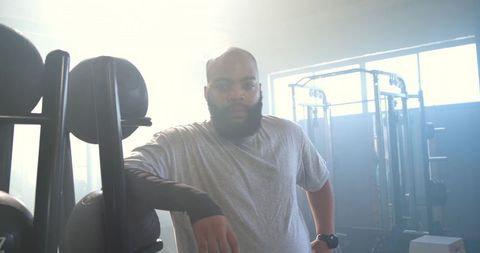 African american man leaning on medicine ball rack in sunlit gym showing focus, strength