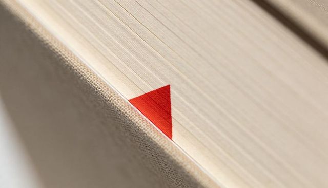 Macro close-up red triangular bookmark tucked into fore-edge of cloth-bound book
