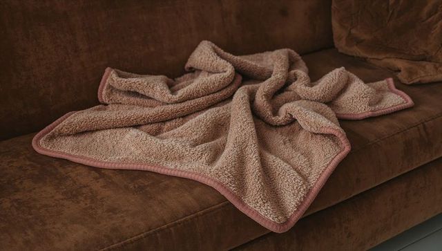 Taupe sherpa throw draping on brown suede sofa with pink trim, cozy plush texture