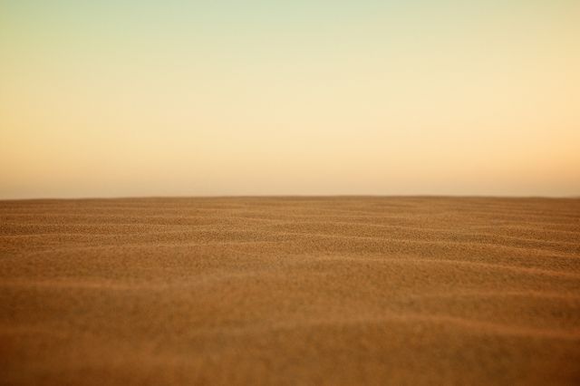 Tranquil scene of pristine desert sand dunes at sunset with a clear sky. Ideal for use in travel promotions, nature documentaries, calming backgrounds, and inspiring minimalist posters or backgrounds.