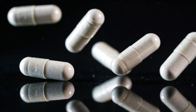 Beige powder-filled capsules reflecting on glossy black surface floating in high contrast