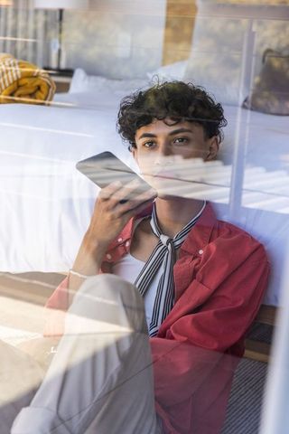 Asian man using smartphone in minimalist bedroom through glass window