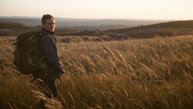 Hiker looking back across golden prairie at sunset with backpack and walking pole