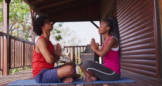 Happy african american couple doing yoga and meditating in log cabin. Freetime, domestic life, countryside and nature concept.