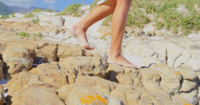 A person is walking barefoot on rocky terrain under bright sunlight, with copy space. Capturing the essence of outdoor adventure, the image evokes a sense of freedom and connection with nature.