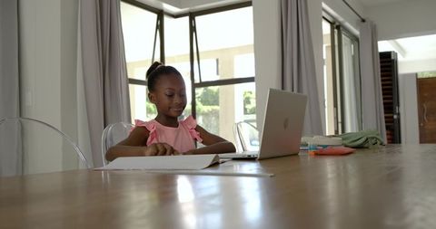 African girl studying at home with laptop and notebook on bright contemporary dining table