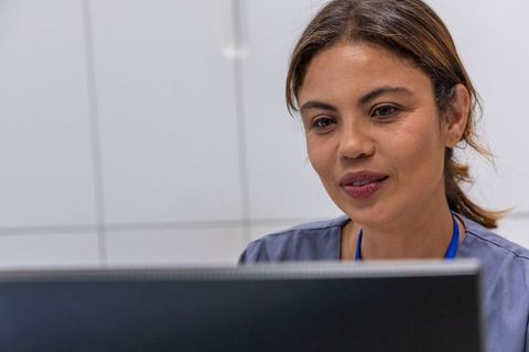 Female clinician working at computer in modern clinic wearing gray scrubs and lanyard