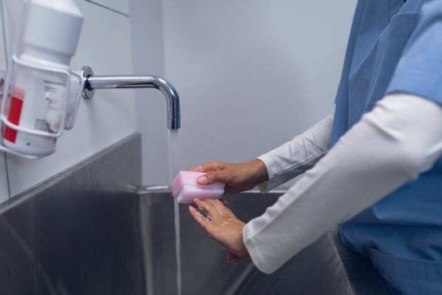 Surgeon washing hands at hospital sink. Emphasizes hygiene and preparation in medical settings. Ideal for use in healthcare, sanitation, and hospital safety presentations or marketing materials.