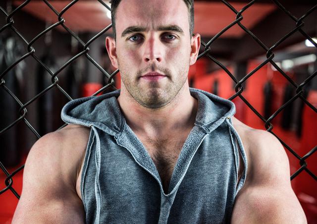 Smart muscular man standing against a fence in fitness studio