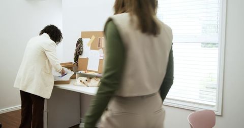 Diverse female designers unpacking materials at bright studio workspace with corkboard