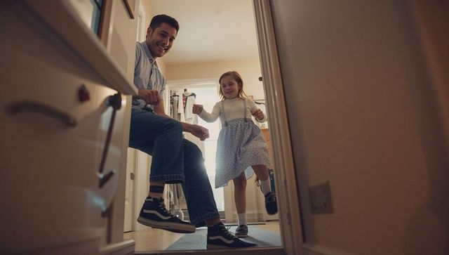 Father watching daughter stepping through doorway on home threshold, playful family moment