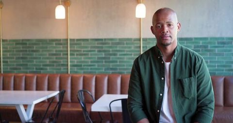 Sitting African man in cafe with green tile wall and banquette, calm coffeehouse portrait