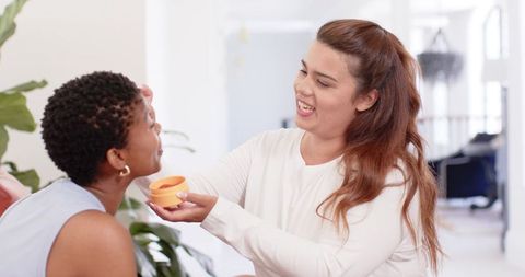 Sharing skincare moment: friends applying moisturizer and laughing at home
