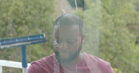 African american man cleaning window with squeegee on porch in maroon t-shirt