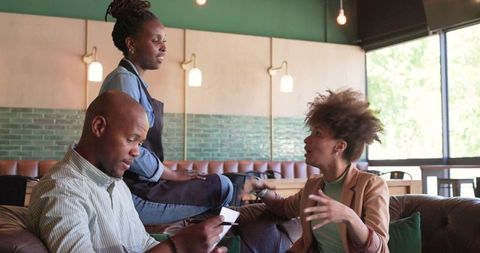 African american server taking order from guests sitting on leather sofa in casual cafe