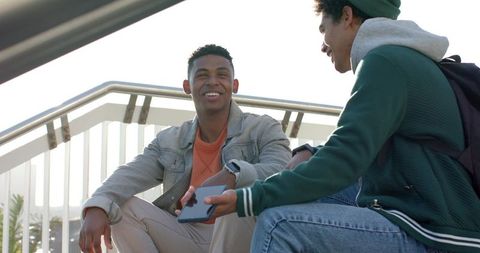 African american friends sitting on outdoor stairs sharing smartphone on college campus