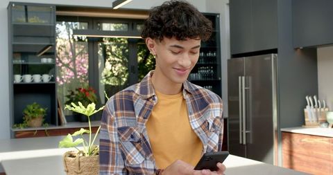 Young Man Using Smartphone in Modern Kitchen with Indoor Plant