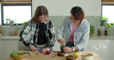 Diverse female friends chopping onions and crushing spices on sunlit wooden kitchen island
