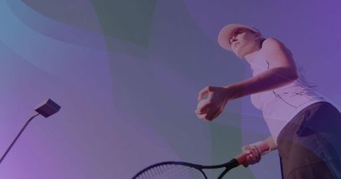 Female athlete serving tennis ball at dusk with cap and tennis racket