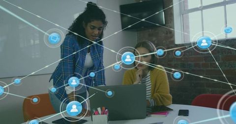 Female Colleagues Collaborating Over Laptop with Digital Network Overlay in Modern Office