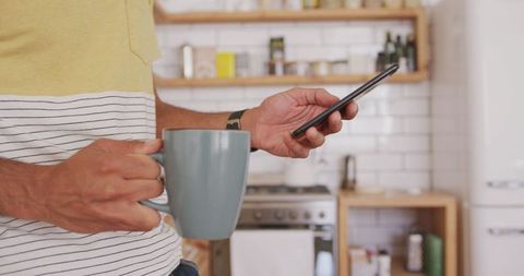 Man Relaxing with Tea Checking Smartphone at Home in Kitchen