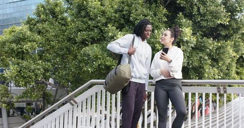 Young friends chatting on urban overpass with duffel bag and smartphone, casual activewear