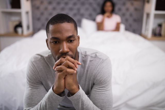 Tensed man sitting while woman lying on bed at home