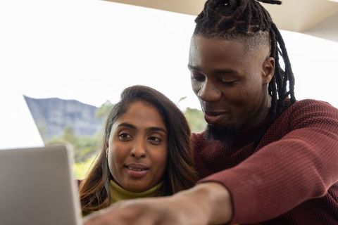 Multicultural couple collaborating on laptop while relaxing on sunlit outdoor terrace