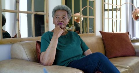 Senior african-american woman sitting on sofa contemplating in cozy sunlit living room
