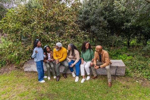 Multigenerational black family relaxing on log bench in park surrounded by greenery