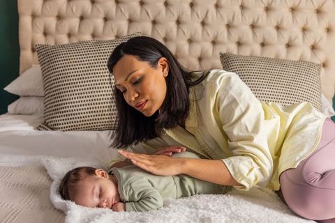 Mother leaning over soothing sleeping baby on bed nurturing newborn care and bonding