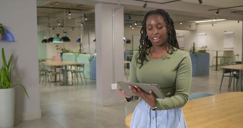 Woman using tablet in contemporary coworking lounge with plants, wooden table, collaboration