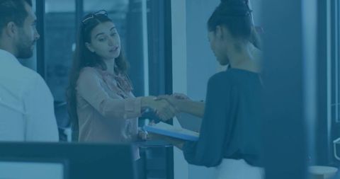 Two Businesswomen Shaking Hands and Exchanging Documents at Office Reception Desk