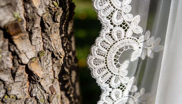 Delicate white lace veil scalloped trim against rustic tree bark close-up wedding detail