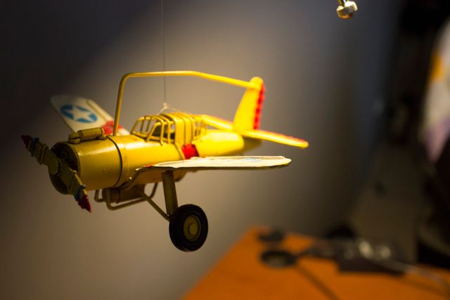 Vintage yellow toy airplane hangs from ceiling in dimly lit room. Perfect for use in educational content on aviation, childhood nostalgia ads, or decorating ideas for playrooms and nurseries.