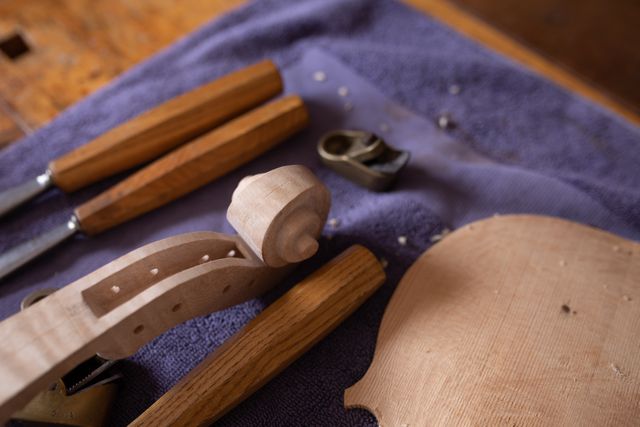 This image depicts a luthier's workbench with an unfinished violin body and various woodworking tools. Ideal for use in articles or advertisements related to musical instrument craftsmanship, woodworking, traditional crafts, and artisan workshops. It can also be used in educational materials about the process of making string instruments.