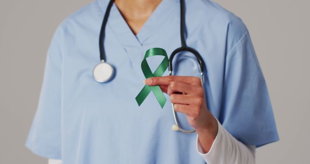 Medical professional in blue scrubs holding a green awareness ribbon, symbolizing support and awareness for health-related causes. Suitable for use in awareness campaigns, healthcare promotions, mental health awareness materials, and charity event advertisements. Highlights the commitment of healthcare workers to various health concerns.